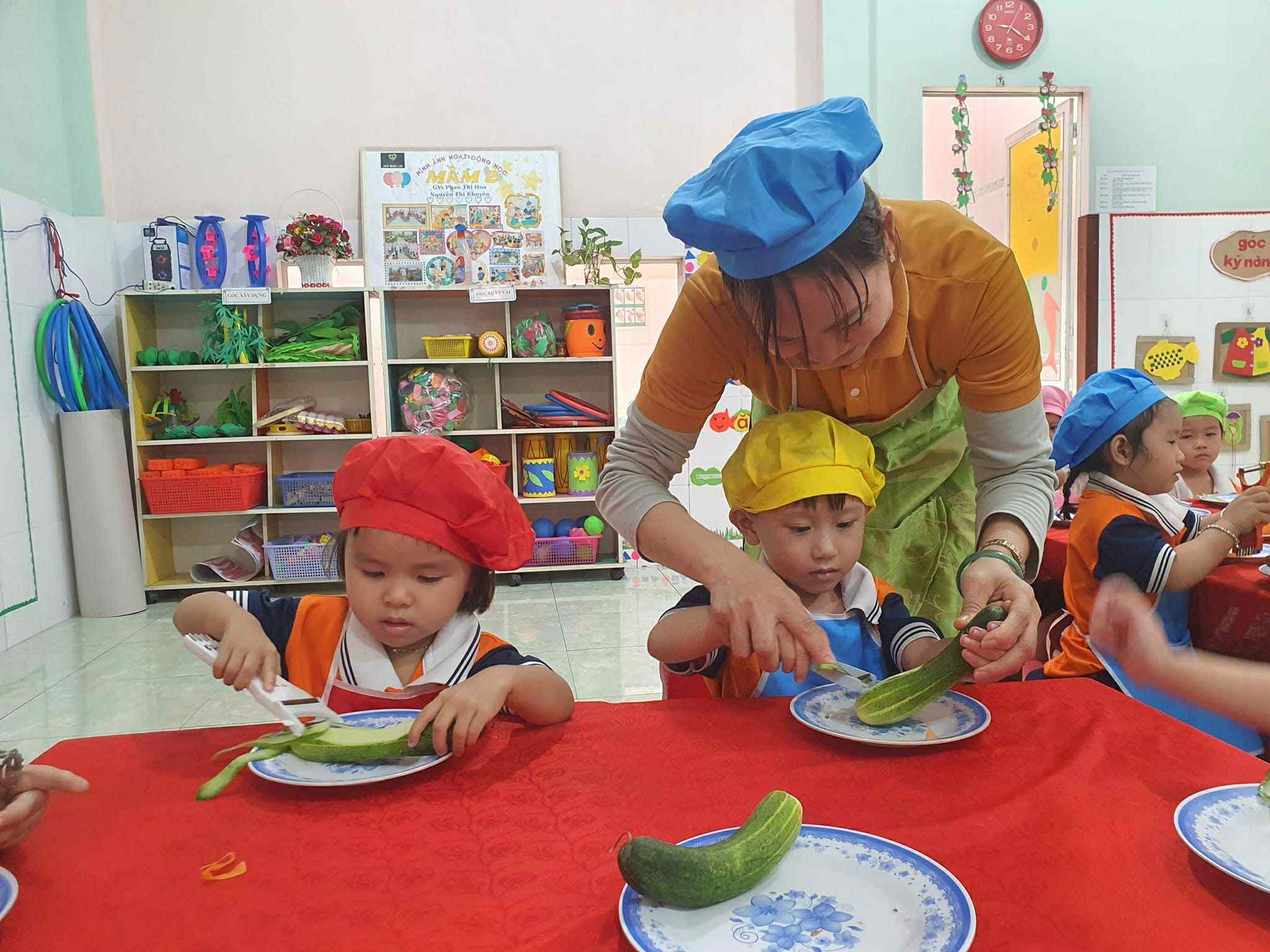 Giáo viên hướng dẫn các bé trải nghiệm hoạt động cắt gọt thực phẩm, rèn luyện kỹ năng khéo léo và hình thành thói quen ăn uống lành mạnh thông qua các tiết học thú vị.